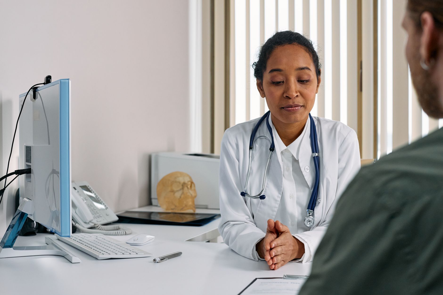 Médica sorridente recebendo paciente em recepção moderna de clínica, com laptop aberto ao fundo simbolizando agendamento online